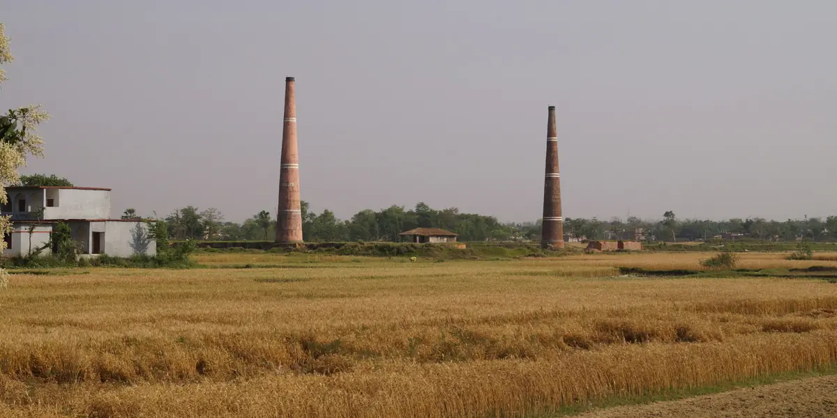 Brick kiln chimneys standing over open farmland on the outskirts of the city, where first-class kiln bricks are fired.
