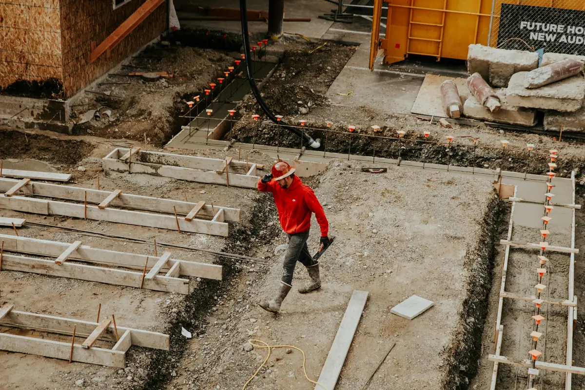 Excavated foundation trenches with formwork set out and a worker levelling the base of a new building.