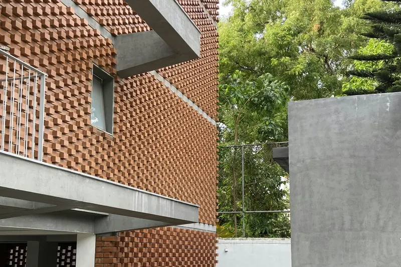 Completed residence with an exposed brick jaali screen wall, concrete band beams and a planted front lawn.