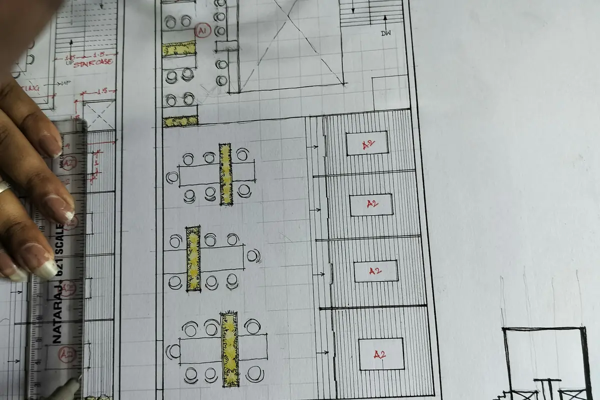 Hand holding a scale rule over an architectural floor plan while measurements are checked.