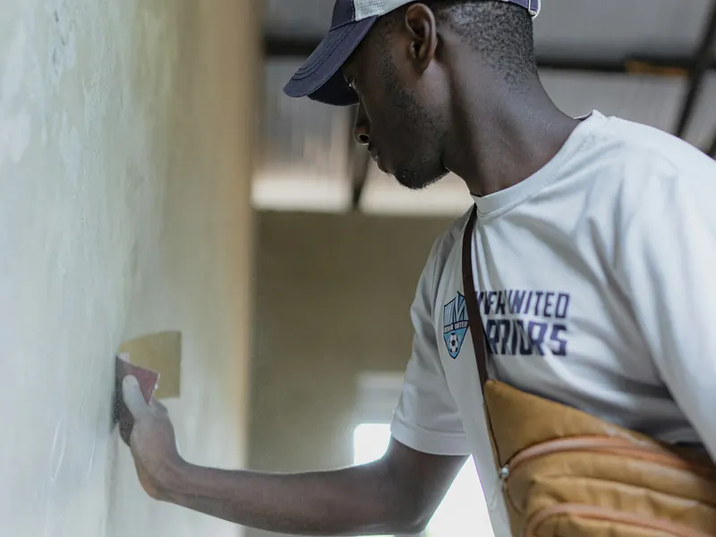 Worker finishing a smooth internal wall surface by hand during the plastering stage of a building.