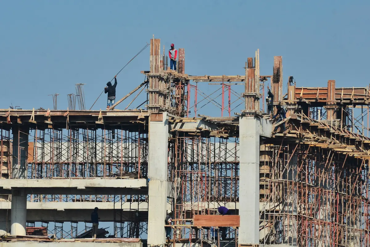Wide reinforced concrete commercial frame under construction, several bays deep, with column starter bars and shuttering in place and workers on the deck.
