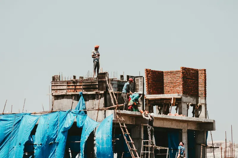 Brick and concrete building under construction with protective sheeting to the lower floor and workers on the upper slab.